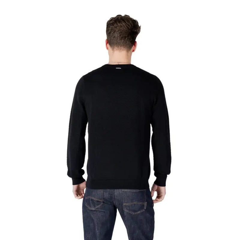 Male model wearing a black long-sleeved sweater paired with dark wash jeans