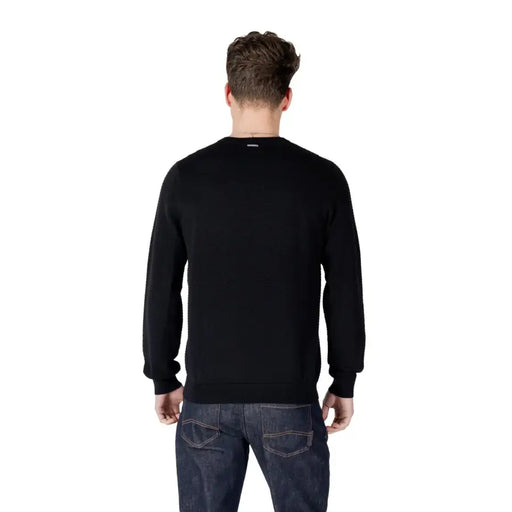 Male model wearing a black long-sleeved sweater paired with dark wash jeans