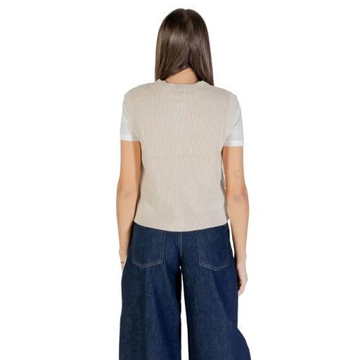 Woman wearing beige ribbed sleeveless gilet with front pockets over a white t-shirt and dark blue wide-leg jeans