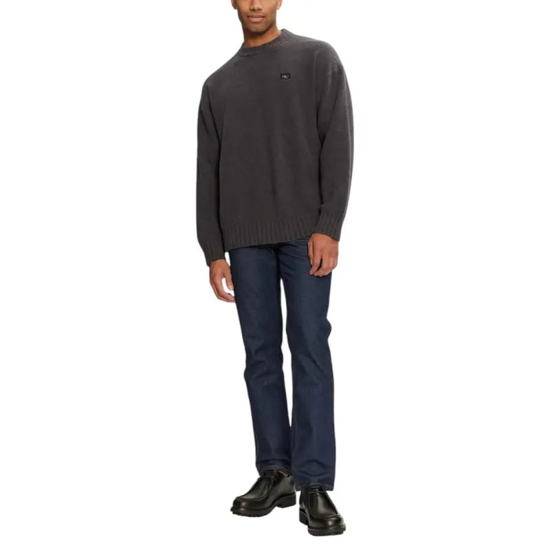 Man wearing gray knit crewneck sweater and dark jeans posing confidently