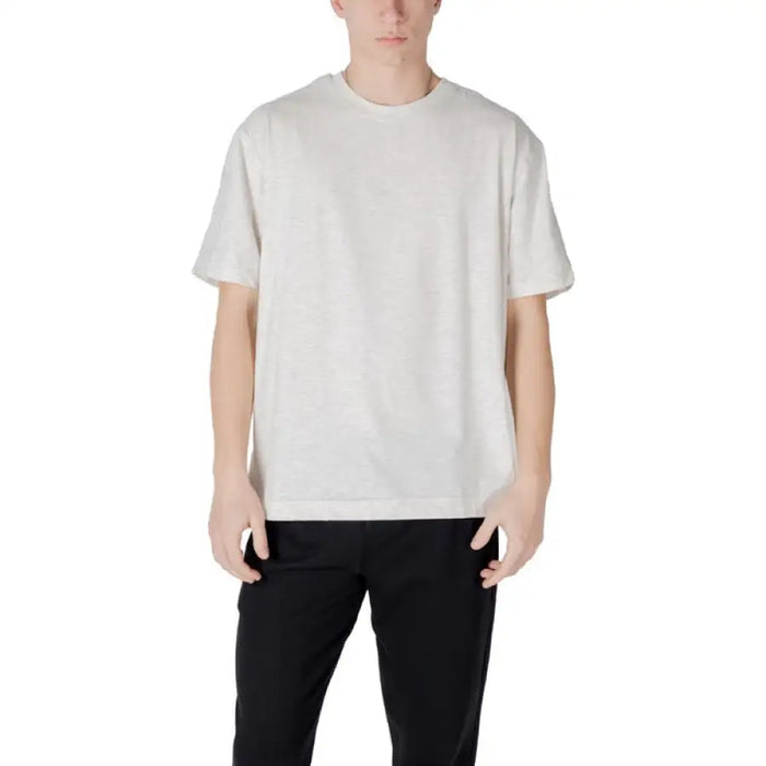 Man wearing a light-colored T-shirt and black pants standing confidently