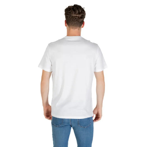 Man wearing Calvin Klein White T Shirt and blue jeans standing against a neutral background