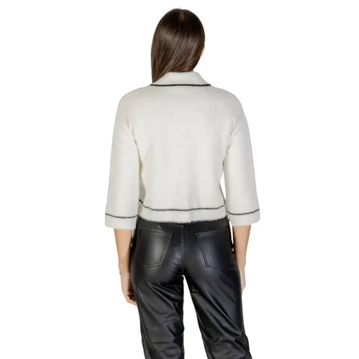 Woman wearing off-white fuzzy cropped cardigan with black trim and black faux leather pants