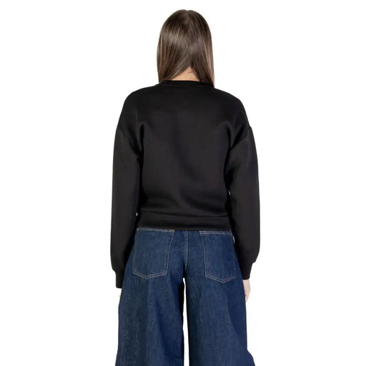 Woman wearing black long-sleeve sweatshirt and dark blue wide-leg jeans in the Only Women Black Long Buttoned Cardigan product image