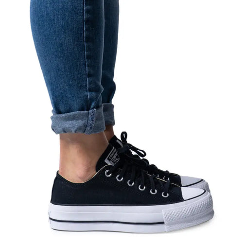 Lower legs and feet wearing cuffed blue jeans and black platform Converse sneakers