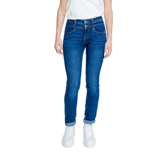 Woman wearing blue high-waisted skinny jeans with cuffed hem and white sneakers