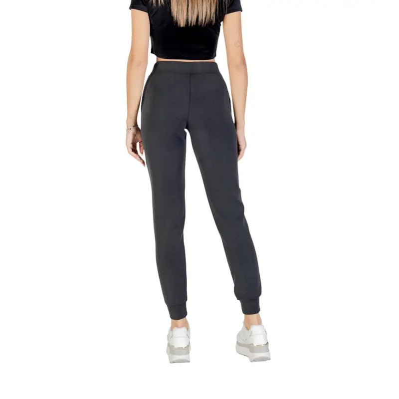 Women wearing Guess Active black crop top and dark grey jogger pants with white sneakers