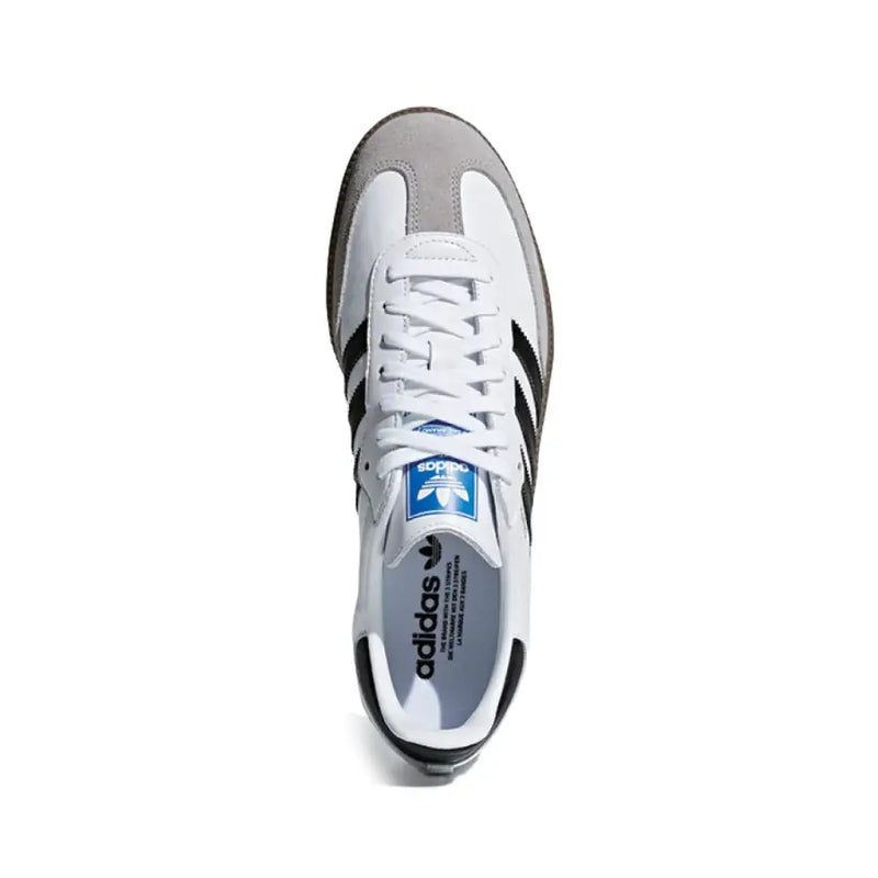 Baskets adidas Samba blanches en cuir avec trois bandes noires, bout renforcé en daim gris, languette arrière et logo adidas bleu sur la languette.