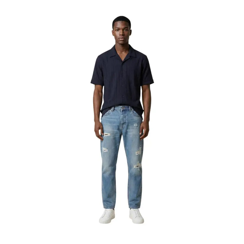 Un jean en denim délavé clair et usé, avec des déchirures aux genoux et aux cuisses, pour homme. Antony Morato