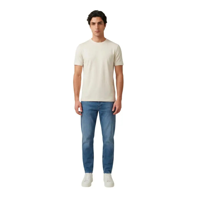 Un homme portant un antony morato hommes t-shirt un t-shirt crème à manches courtes et col rond, porté avec un jean bleu délavé.