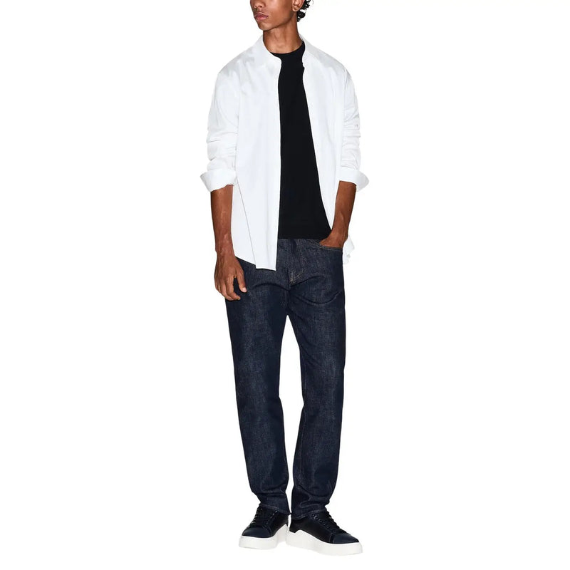 Un homme portant un Armani Exchange T-shirt noir en coton pour homme, porté avec une chemise blanche, un jean bleu foncé et des baskets noires.