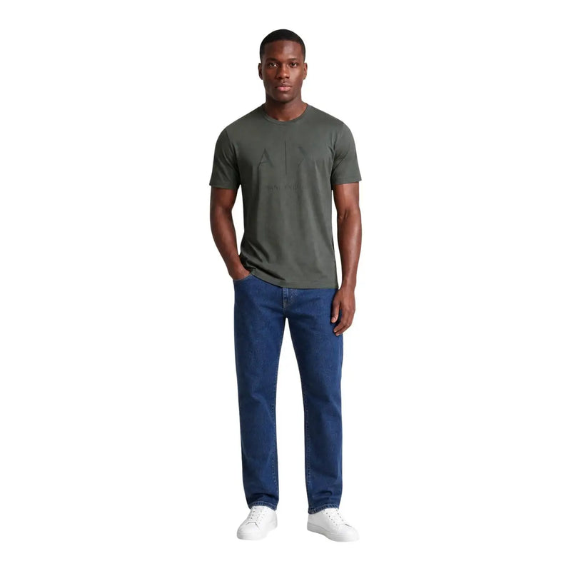 Un homme portant un Armani Exchange T-shirt vert en coton pour homme avec détails graphiques noirs, porté avec un jean bleu et des baskets blanches.