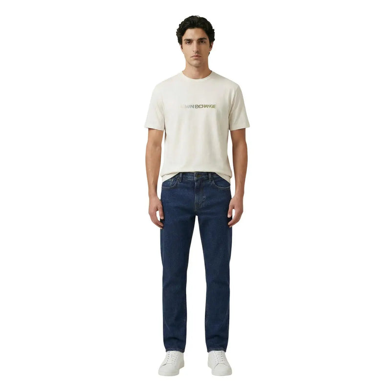 A man wearing a cream-colored Armani Exchange men t-shirt with subtle gold lettering and dark blue denim jeans