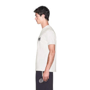 Armani Exchange T-shirt blanc en coton pour homme, manches courtes, logo circulaire noir, porté avec un pantalon bleu marine brodé.