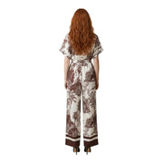 Une femme porte une combinaison Artigli beige en viscose à imprimé floral marron, manches papillon et jambes larges.