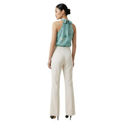 Une femme portant un pantalon Artigli blanc crème à poches zippées sur le devant et un haut dos nu en soie turquoise. top avec un nœud dans le dos