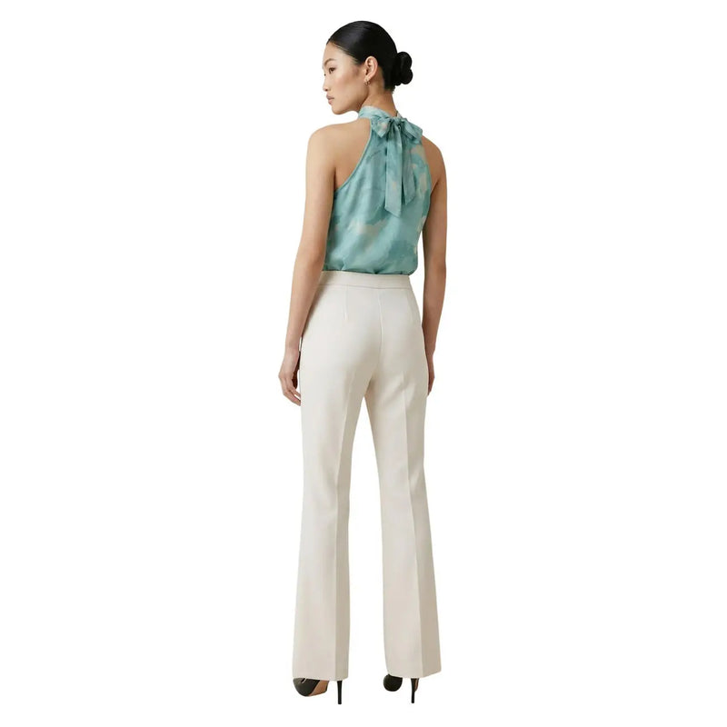 Une femme portant un pantalon Artigli blanc crème à poches zippées sur le devant et un haut dos nu en soie turquoise. top avec un nœud dans le dos