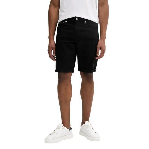 Men wearing black denim shorts paired with a white T-shirt in a fashion display