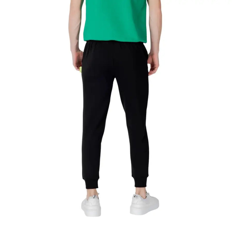 Black sweatpants with elastic cuffs white drawstring and subtle yellow tag on the side seam in comfortable jogger style