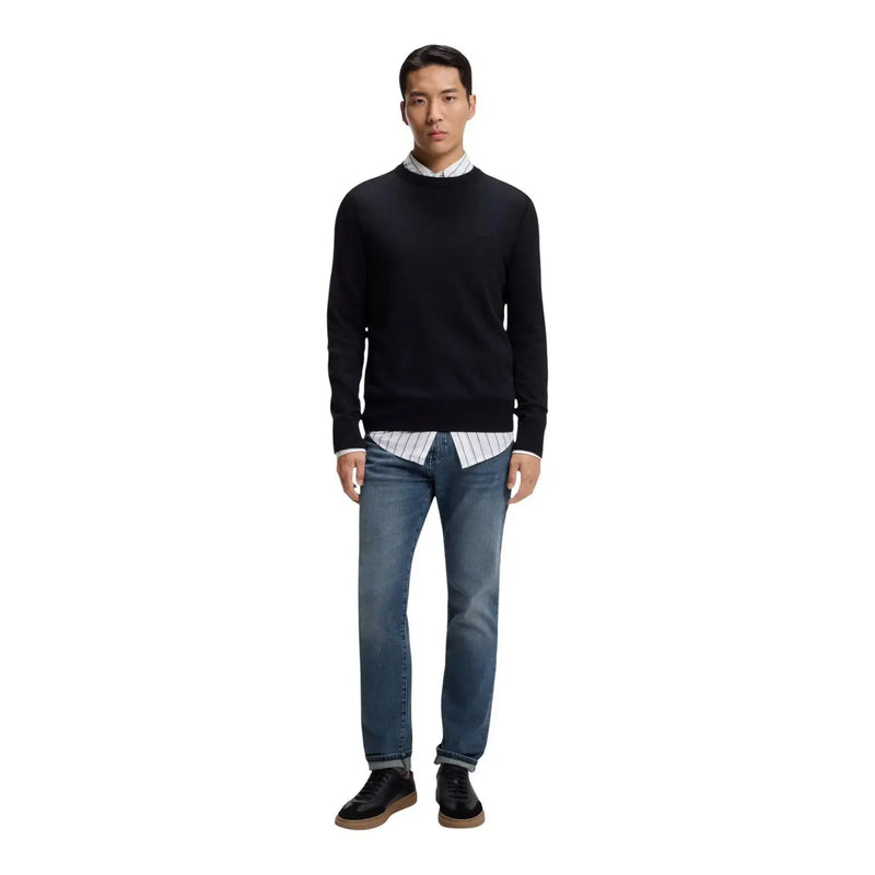 Pull ras du cou Boss Jeans noir pour homme, avec poignets et ourlet côtelés, porté sur une chemise rayée à col, par un mannequin.