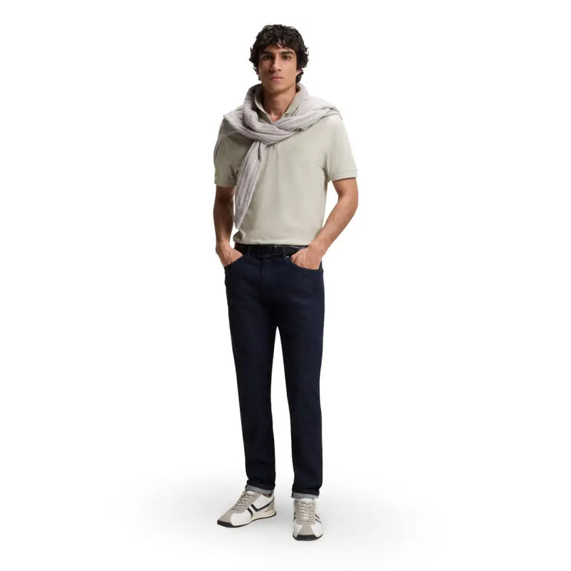 Un homme portant un polo gris en coton à col zippé et manches courtes de marque Boss Men, un jean slim bleu marine et des baskets blanches.