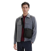 Sac bandoulière noir pour homme en polyuréthane, au design minimaliste et élégant, avec un logo discret. Dimensions : 16 x 22 x 6 cm.