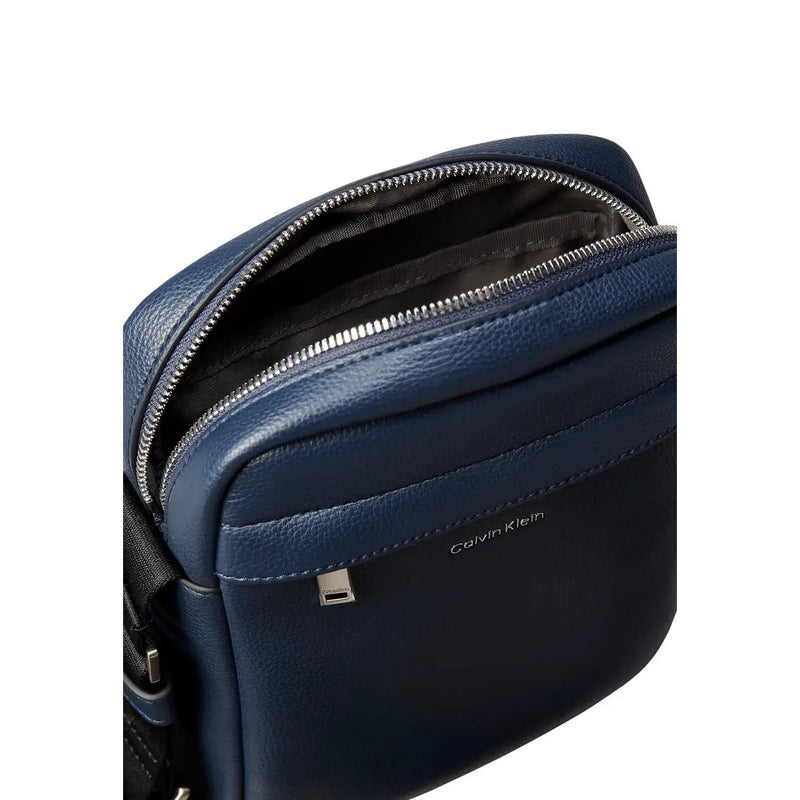 Calvin Klein Sac bandoulière Raised Reporter pour femme en cuir bleu foncé avec fermeture éclair argentée et surpiqûres discrètes, vue de face