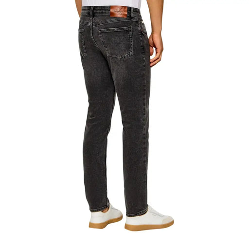 Calvin Klein Jean homme en denim gris foncé délavé et usé, avec étiquette de marque en cuir marron à la ceinture.