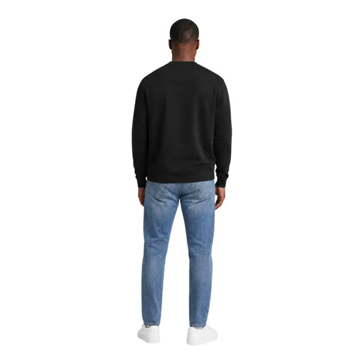 Sweat-shirt noir en coton à col rond et manches longues, porté avec un jean bleu clair. Calvin Klein Jeans hommes