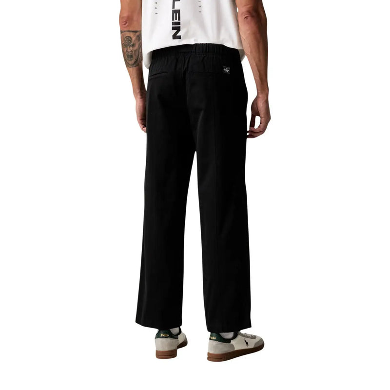 Pantalon Calvin Klein Jeans pour homme, en coton noir, jambes larges, coupe décontractée, taille élastique et logo discret sur la poche arrière.