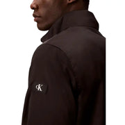 Calvin Klein Jeans Blazer noir zippé pour homme, en polyester légèrement brillant, avec un écusson logo blanc contrastant sur la poitrine gauche.