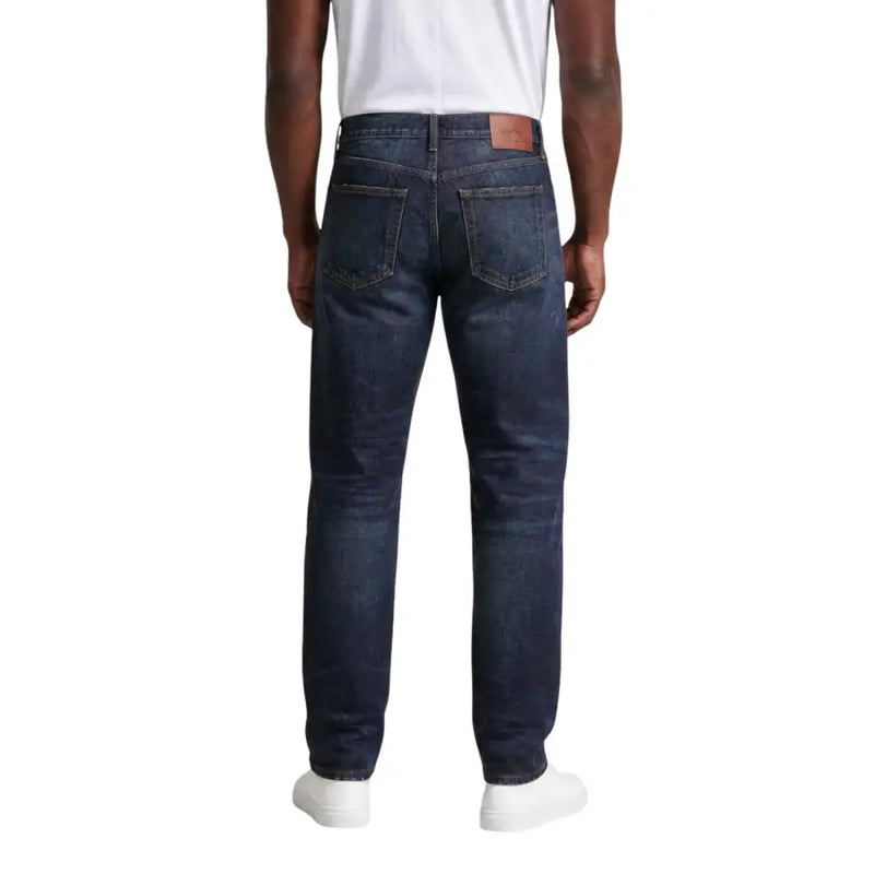 Jean en denim de coton indigo foncé avec une coupe classique à cinq poches et un écusson de marque en cuir marron sur la ceinture. Calvin Klein Jeans