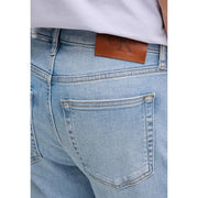 Vue arrière d'un jean Calvin Klein pour homme, en denim de coton bleu clair, avec un écusson de la marque en cuir marron sur la ceinture.