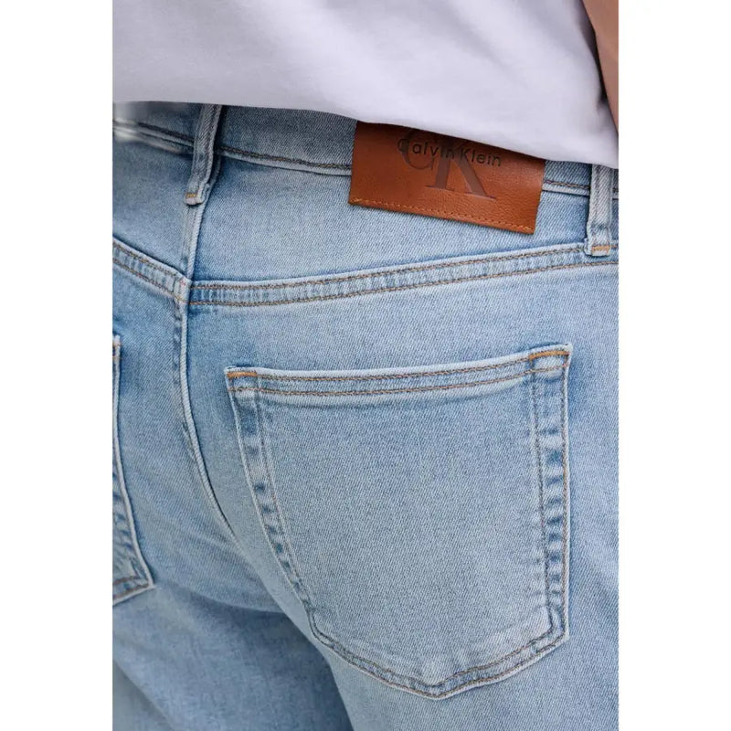 Vue arrière d'un jean Calvin Klein pour homme, en denim de coton bleu clair, avec un écusson de la marque en cuir marron sur la ceinture.