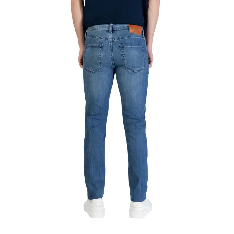 Jean Calvin Klein pour homme, en denim de coton bleu, coupe slim classique, avec empiècement en cuir marron à la ceinture (vue de dos).