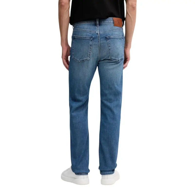 Vue arrière d'un jean Calvin Klein pour homme, en denim de coton bleu, coupe droite, avec un écusson de la marque en cuir marron.