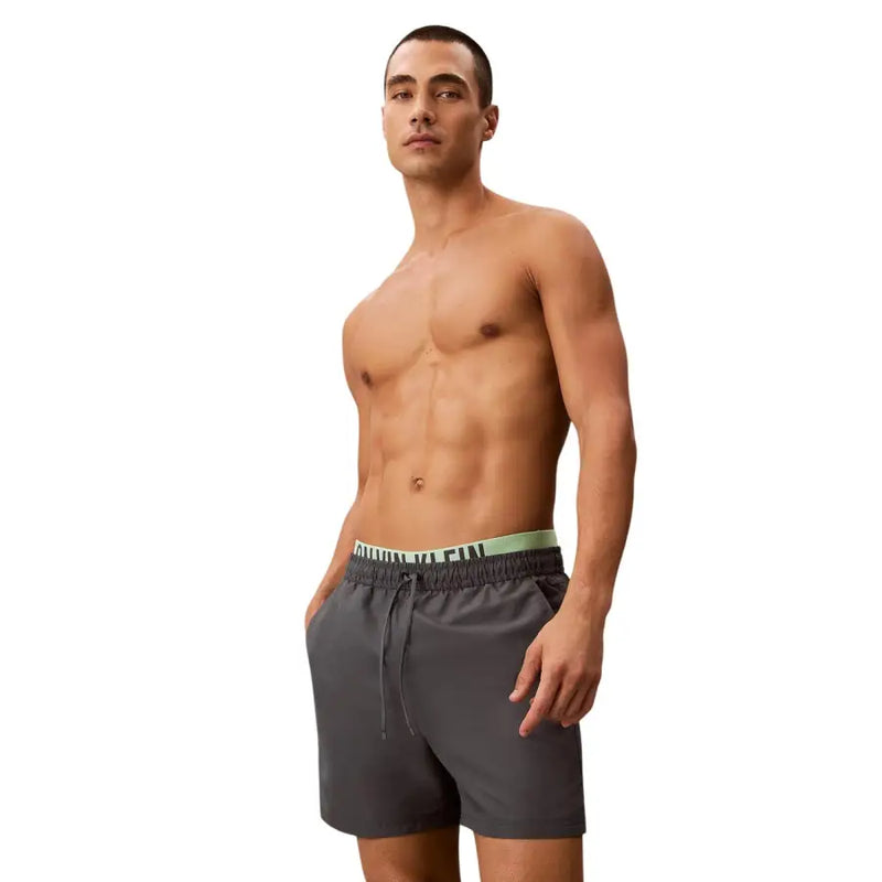 Dark gray Calvin Klein Jeans men swimwear trunks with light green waistband and black logo lettering