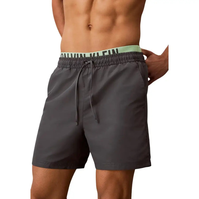 Dark gray Calvin Klein Jeans men swim trunks with light green waistband and black brand logo for swimwear use