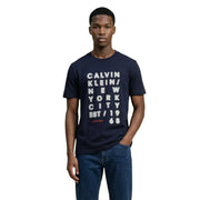 bleu marine Calvin Klein Jeans hommes t-shirt avec un graphisme graphique vertical blanc gras et le nom de la marque en lettres rouges sur le devant