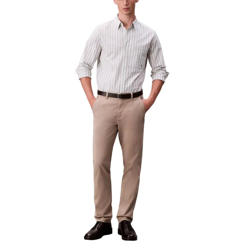 Un homme portant un pantalon chino beige à manches retroussées et des chaussures noires avec Calvin Klein Jeans pantalon noir en coton élasthanne