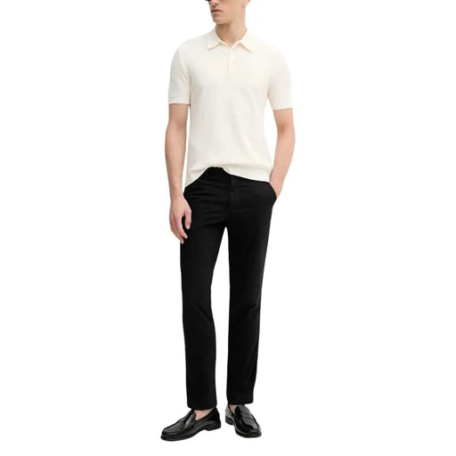 Calvin Klein Jeans Pantalon pour homme porté avec un polo en maille côtelée couleur crème, à col classique et manches courtes.