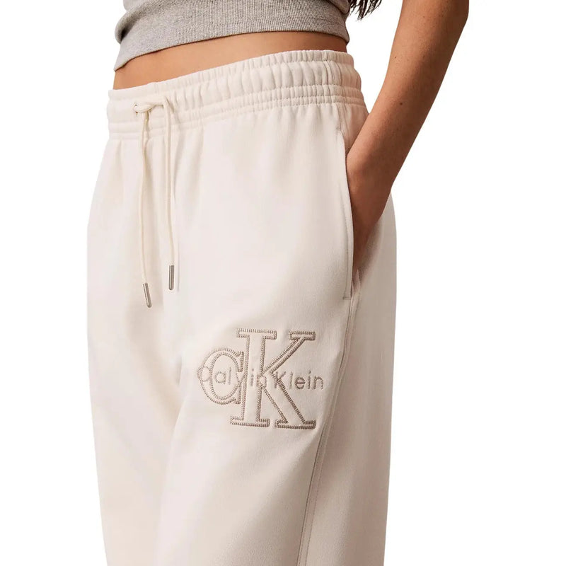 Pantalon de survêtement Calvin Klein pour femme, couleur crème, en coton blanc, avec logo brodé texturé et détails en dentelle sur la cuisse.