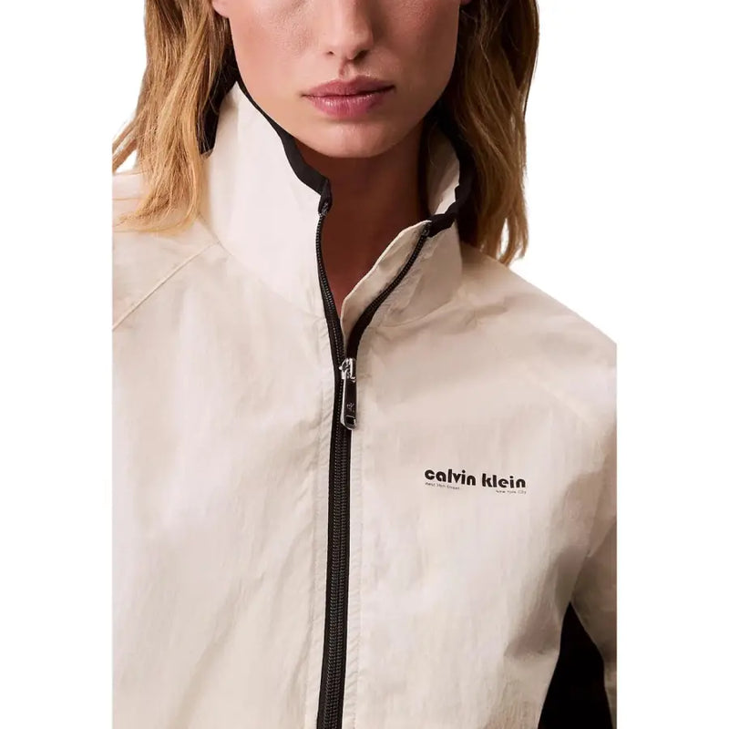 Cream-colored calvin klein windbreaker with black zipper and trim shown with calvin klein jeans women white turtleneck blazer