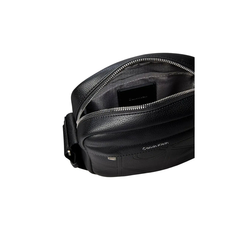 Sac bandoulière Calvin Klein en cuir noir texturé avec fermeture éclair argentée, modèle reporter, dimensions L 16 x H 20 cm