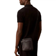 Sac bandoulière Calvin Klein pour homme en cuir noir perforé avec fermeture éclair argentée et logo de la marque (vue de face)