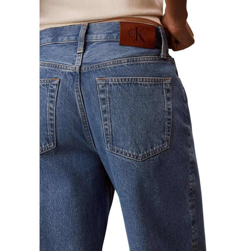 Jean Calvin Klein pour femme en denim de coton bleu, dos visible, avec un écusson de la marque en cuir marron à la taille.