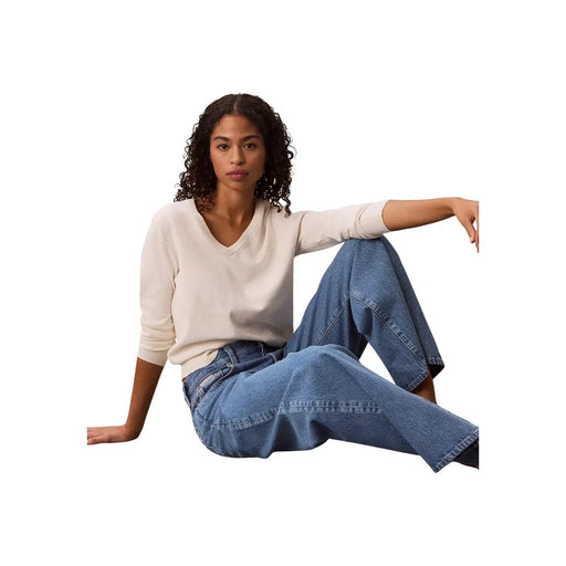 Femme portant un jean large en coton bleu Calvin Klein et un pull crème à col en V (vue de face)