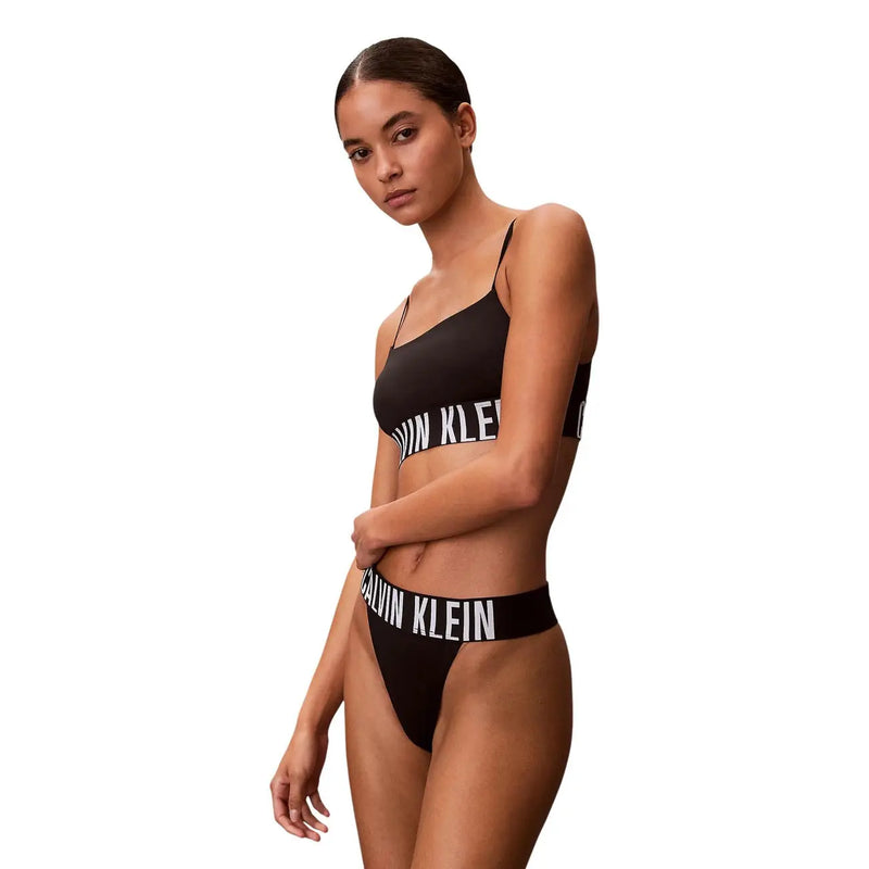 Ensemble bikini string noir Calvin Klein pour femme, échancré, avec inscription blanche, en polyester et élasthanne.
