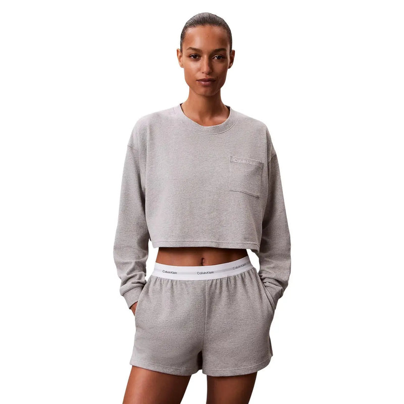 Sweat-shirt court gris avec petite poche poitrine ornée du logo Calvin Klein, porté avec un short en jersey de coton noir.