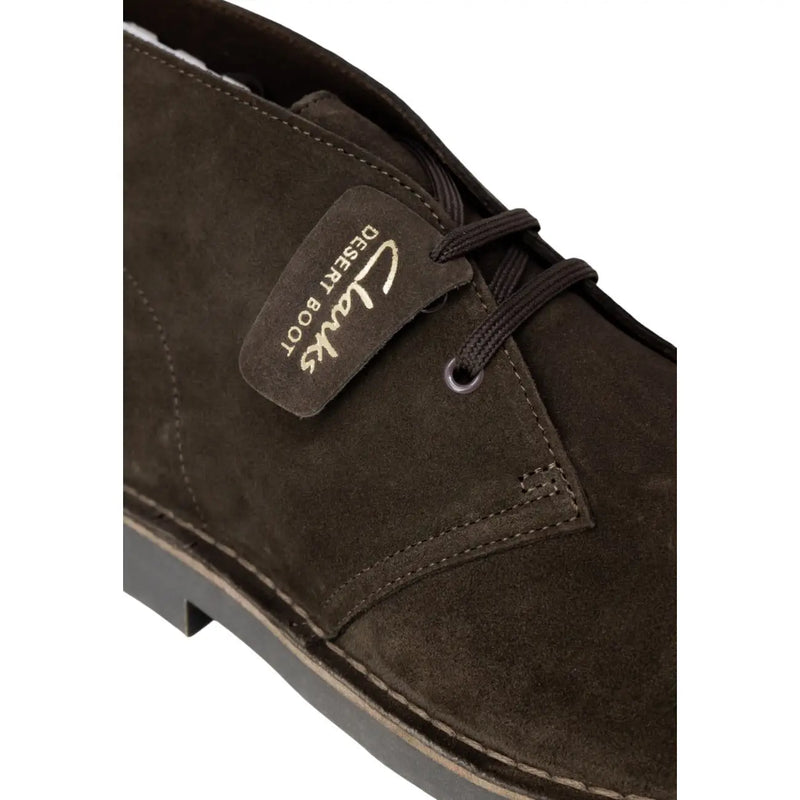 Bottines Clarks pour homme en cuir marron, style désert en daim marron foncé, avec lacets noirs et étiquette en cuir cousue.